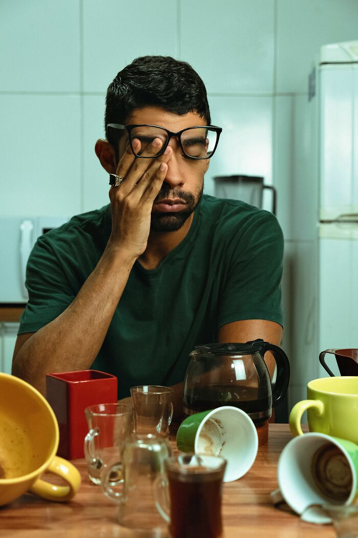 Tired man with anxiety sitting at table with coffee cups and pot