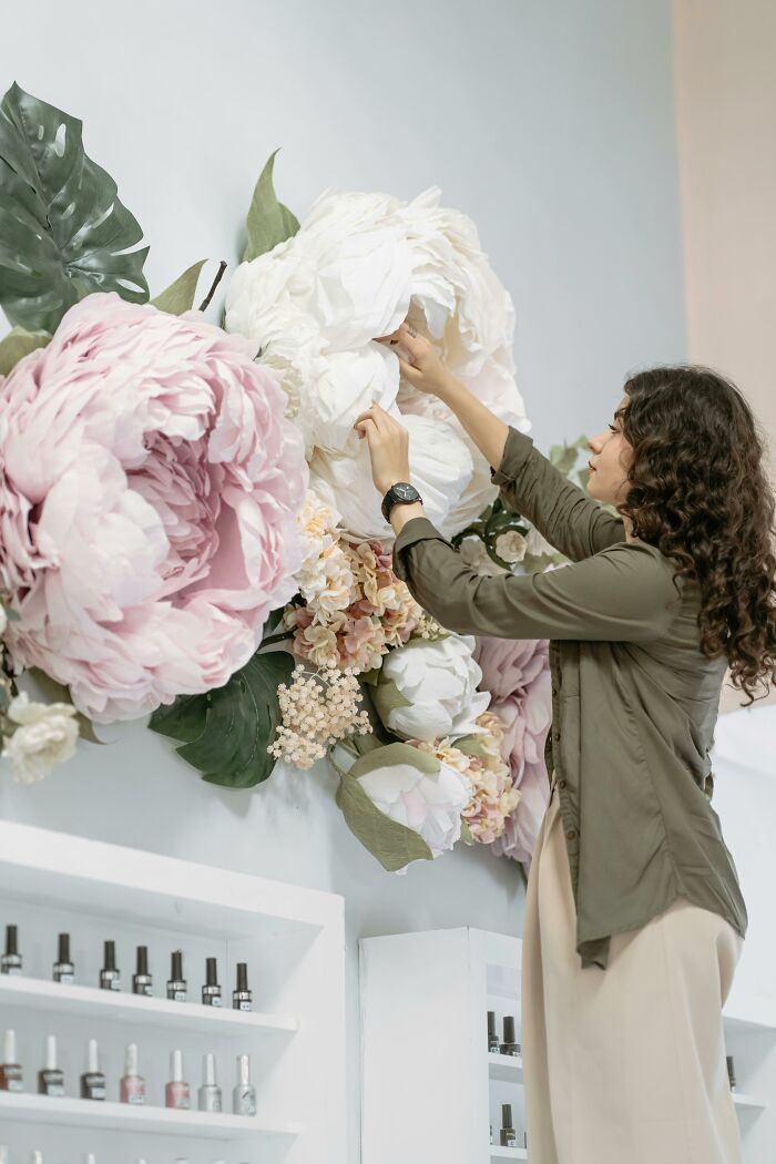 Woman arranging large artificial flowers on wall