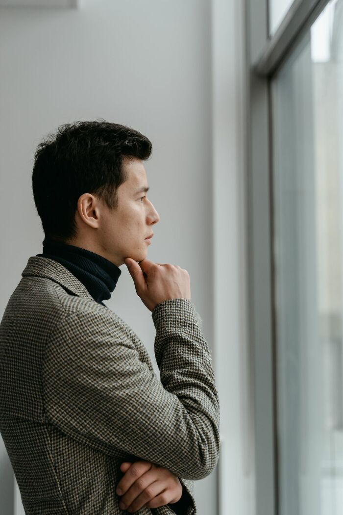 A man in a turtleneck and blazer looks contemplatively out a window, reflecting on polygamous family stories.