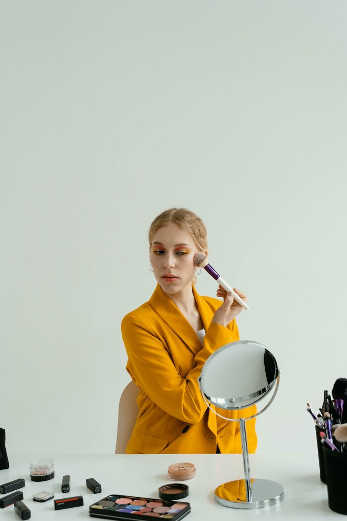Young woman applying makeup with brush in yellow blazer
