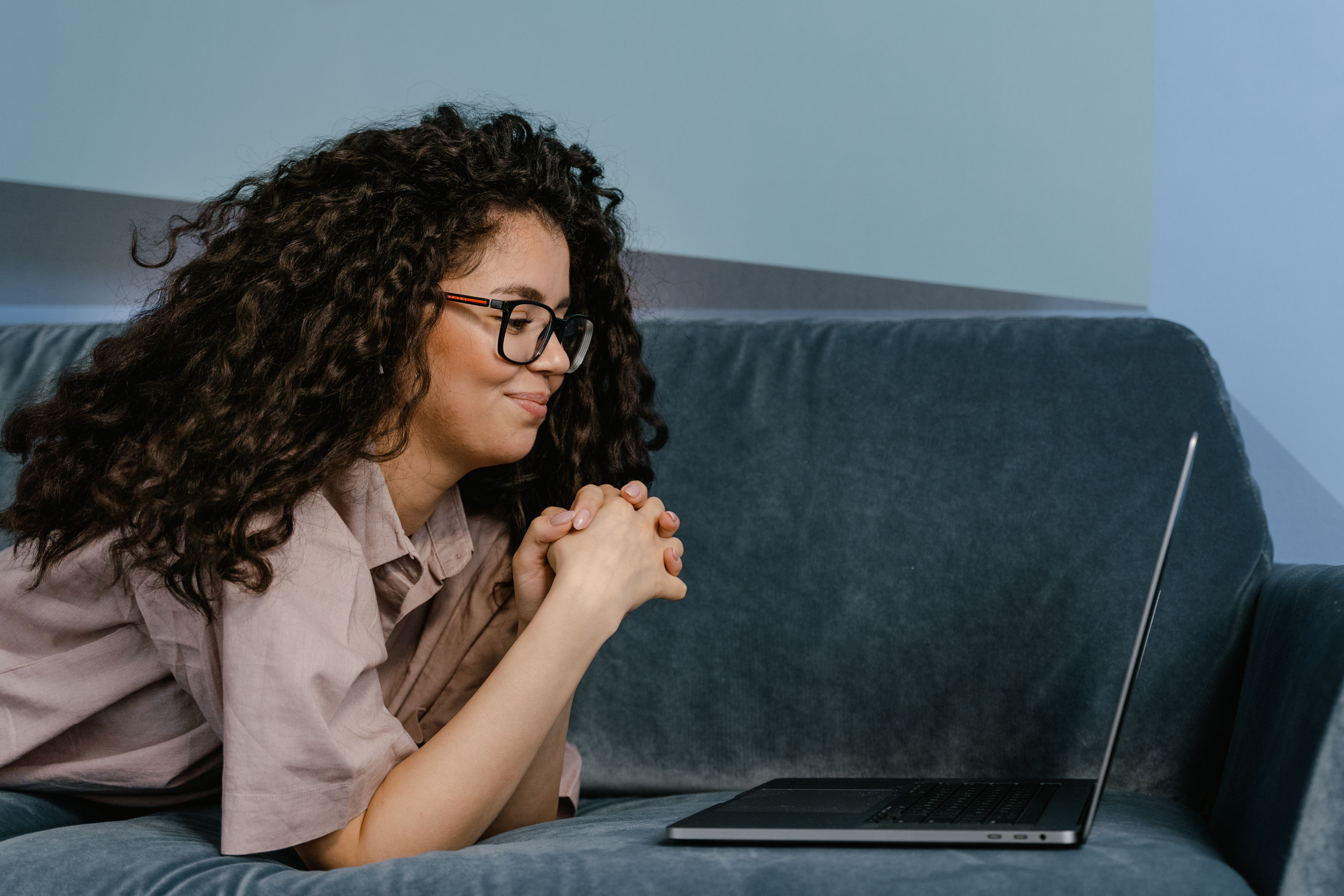 A woman smiling while looking at a laptop on a couch, after her ex tried to embarrass her.