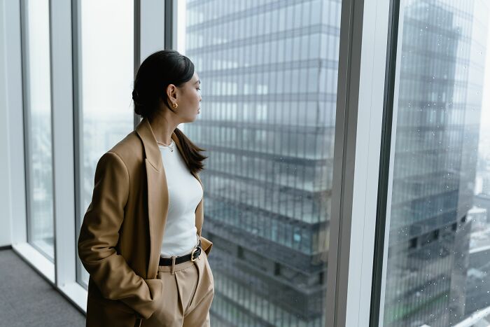 A woman in a business suit looks out a window at a city skyline, perhaps feeling she simply couldn't take it anymore and snapped.