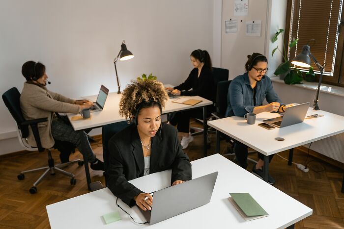 Four office workers wearing headsets and typing on laptops in an open-plan office, illustrating a rage mode at work.