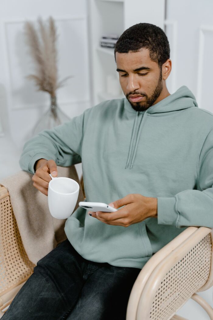 Man checking phone with concern while holding coffee at home