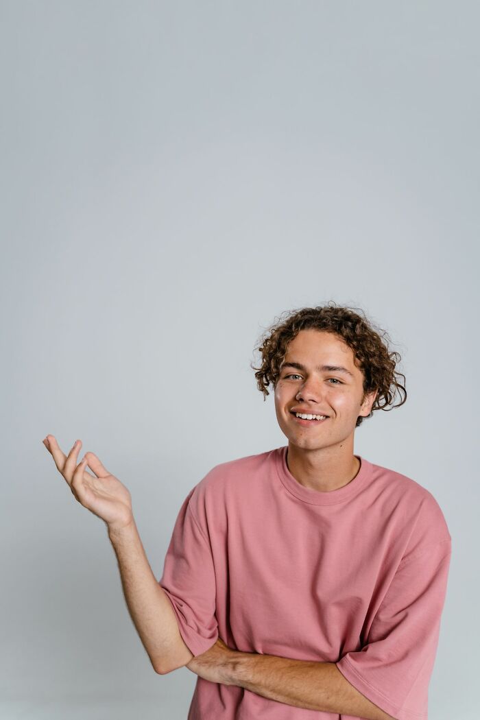 A young man with curly hair and a pink shirt, a modern representation in a story about polygamist families.