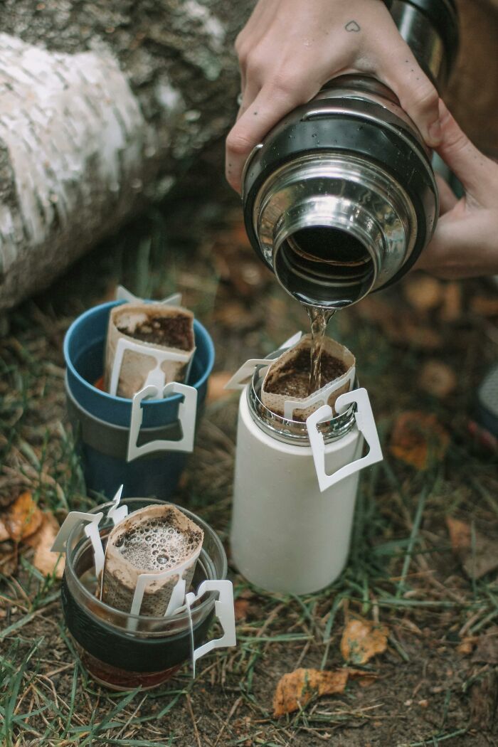 Pouring hot water from a thermos into drip coffee filters outdoors