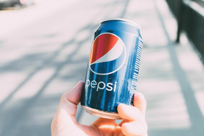 A hand holding a can of Pepsi outdoors, a typical beverage experience when visiting the US.