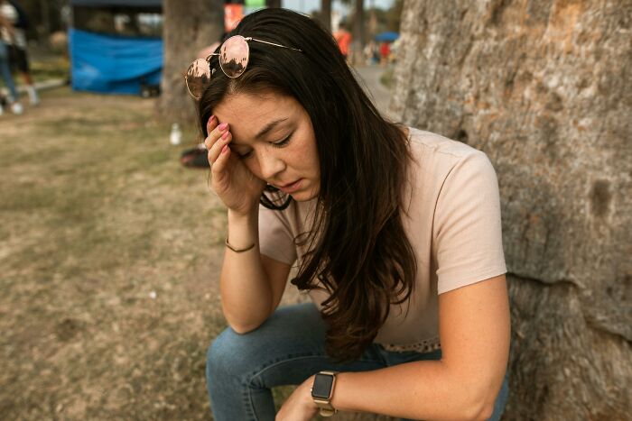 Stressed woman sitting outdoors looking worried and exhausted