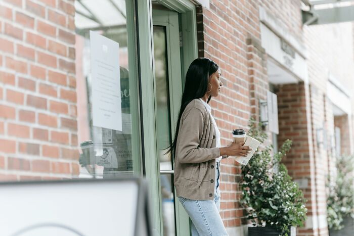 Woman stepping out of cafe holding coffee in a moment of simple generosity