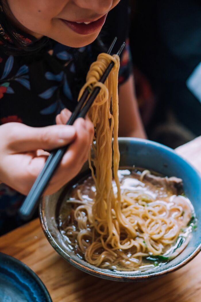 A person using chopsticks to eat noodles from a blue bowl, illustrating an experience that may lead to an unserious ER visit.