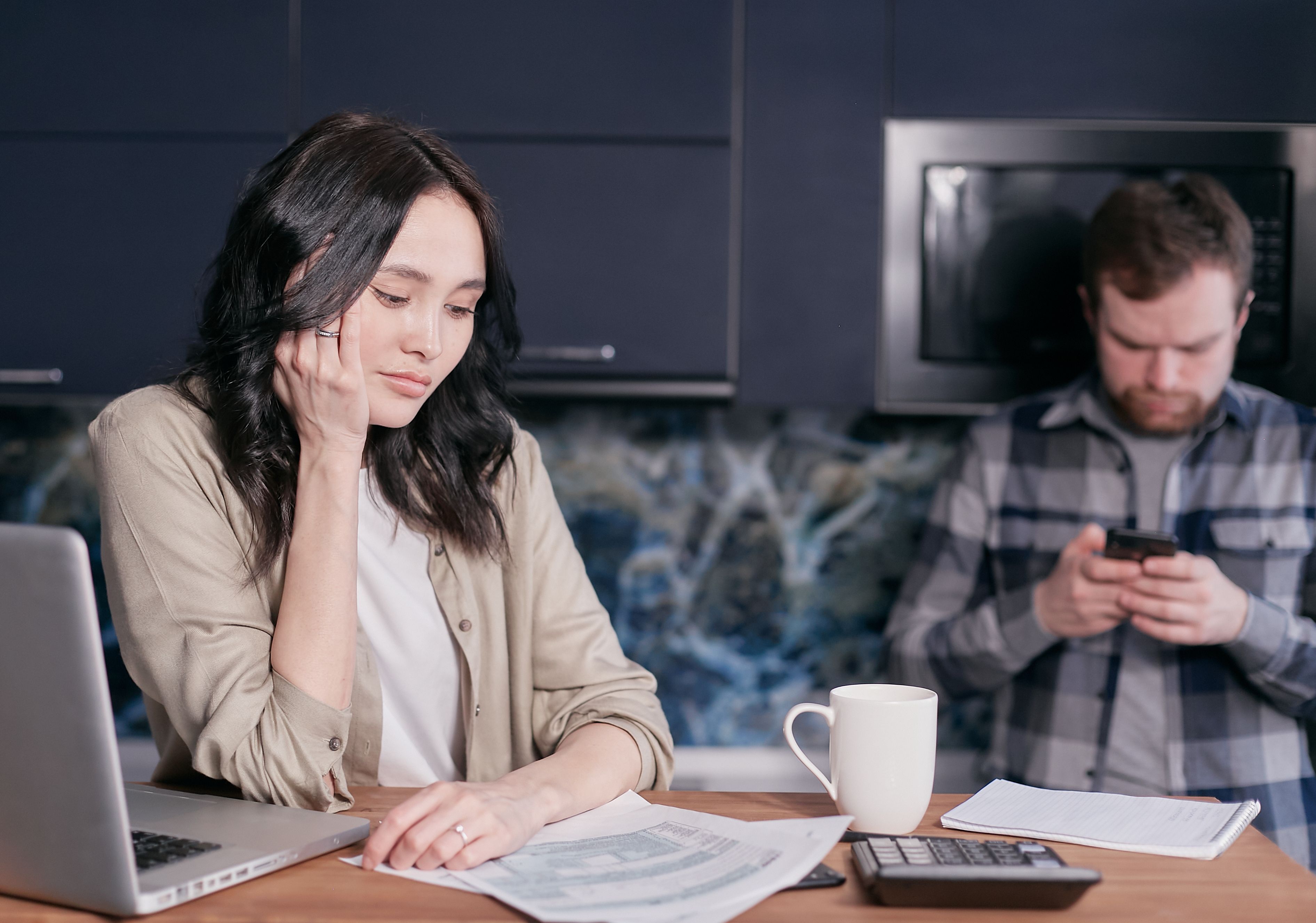 Worried wife dealing with unemployment while husband focused on AI on his phone in kitchen Worried wife dealing with unemployment while husband focused on AI on his phone in kitchen