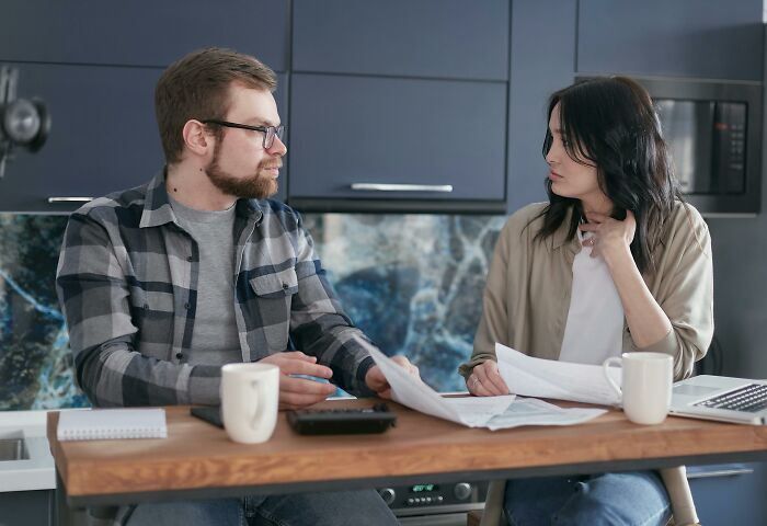 Couple sitting at kitchen table discussing documents with tense expressions