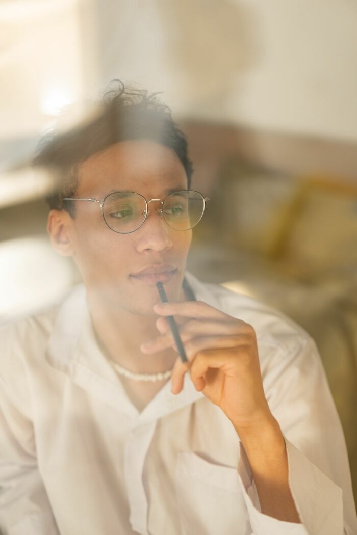 A pensive man in glasses holding a pen to his lips, revealing hints of a person who is secretly very smart.