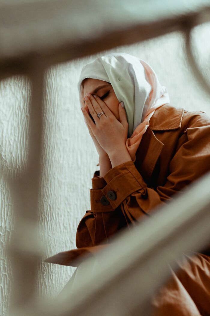 A woman wearing a hijab, covering her face in distress, symbolizing stories from polygamist families.