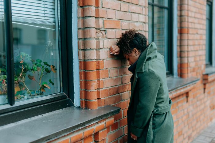 Woman leaning head on brick wall showing frustration related to entitled parents