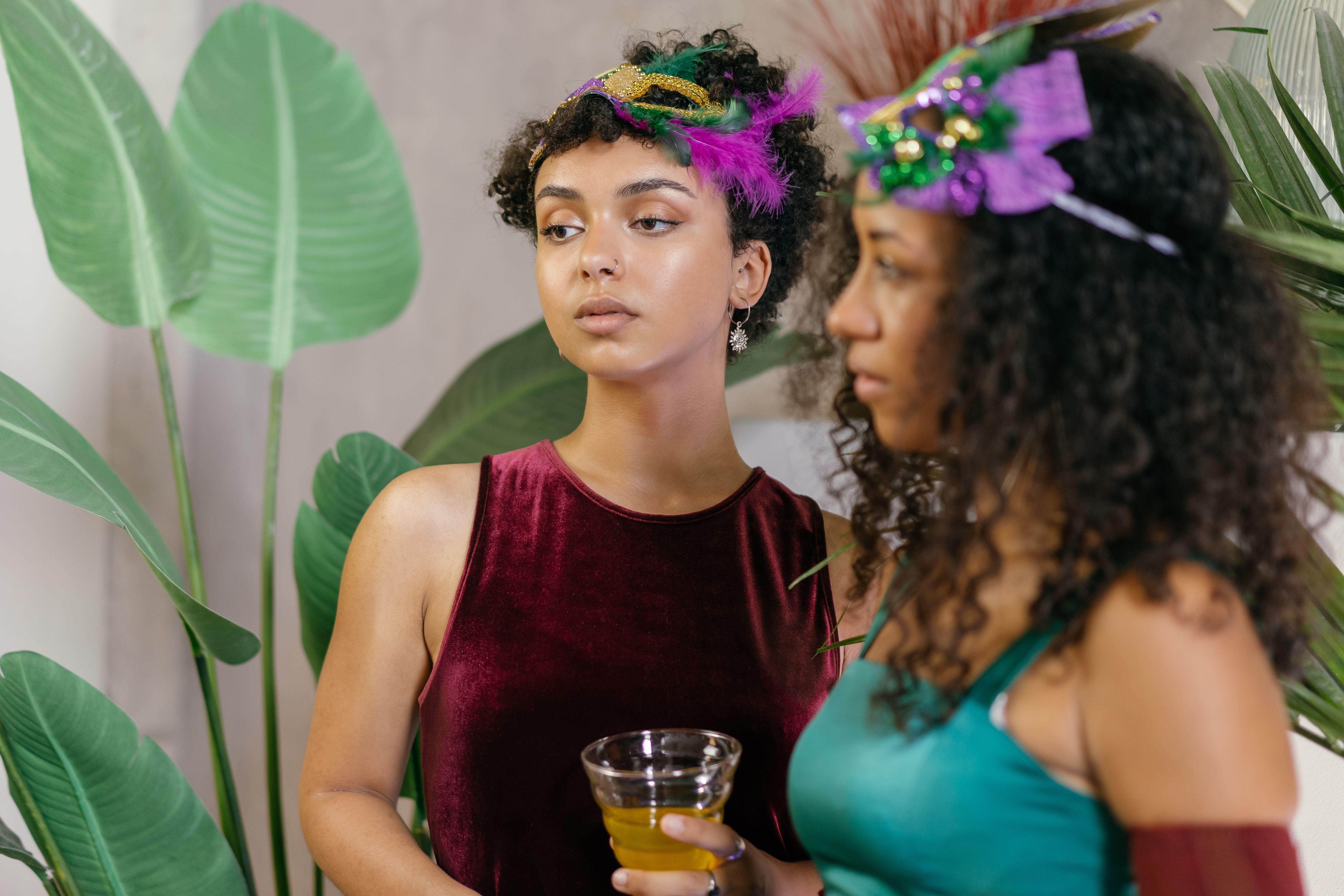 Two women wearing feathered masks in a tense moment at a wedding