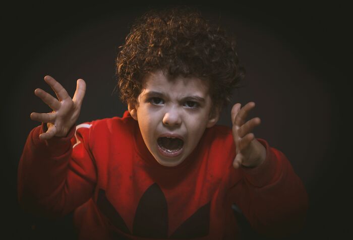 A young child with curly hair in a red shirt, screaming with hands raised, illustrating someone in full rage mode.