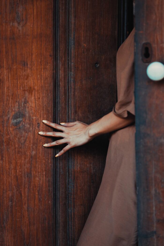 A woman in a brown dress with yellow painted fingernails touching an old wooden door, depicting experiences people can't explain.