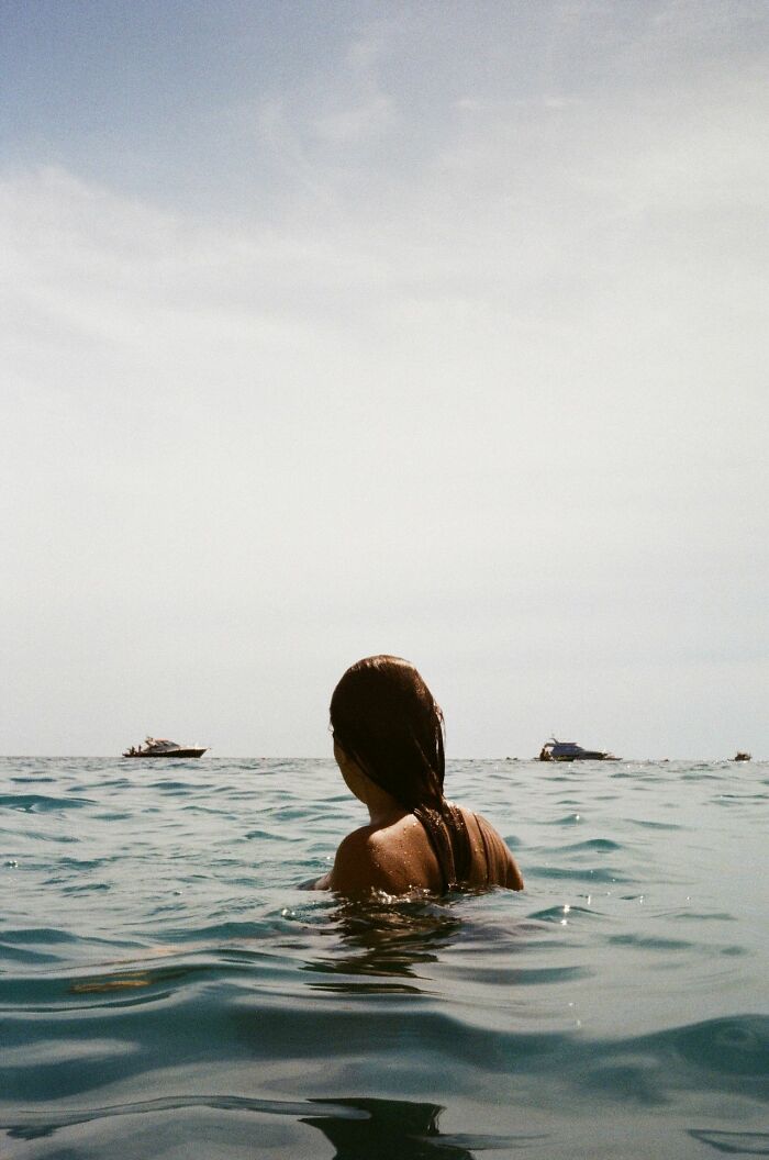 Woman swimming in ocean with boats in the distance