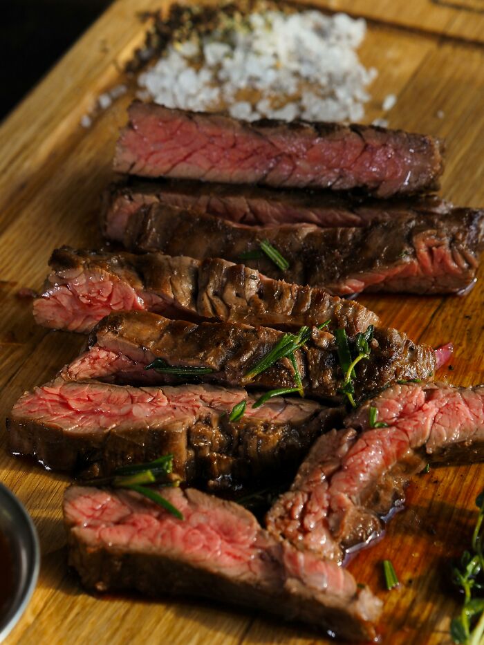 Slices of medium-rare grilled steak garnished with herbs on wooden board
