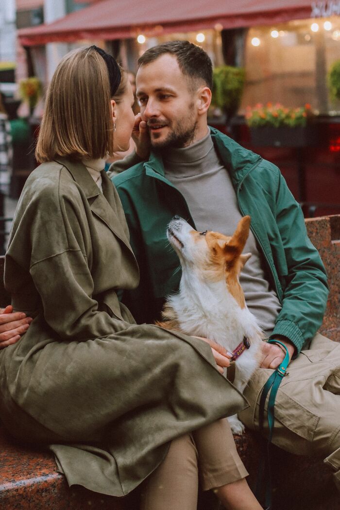 A couple sits on a bench with their corgi, highlighting human habits that confuse dogs.