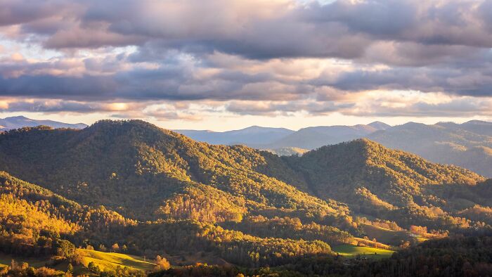 Rolling hills covered in autumn trees under a dramatic cloudy sky, highlighting interesting and surprising facts of natural landscapes.