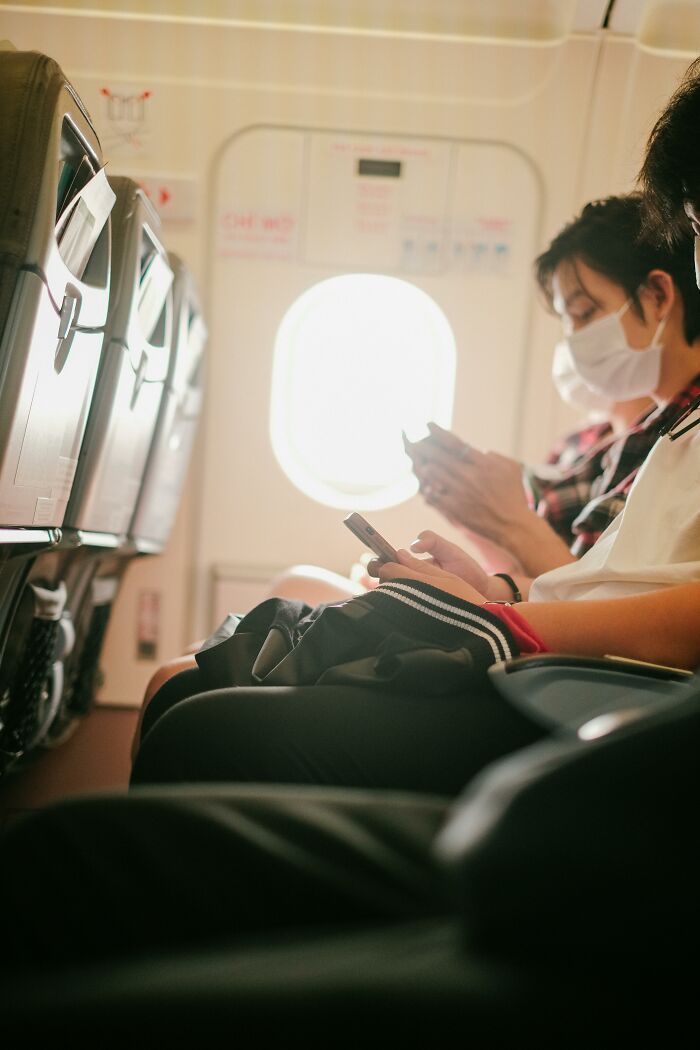 Plane passengers wearing masks using smartphones during flight safety briefing