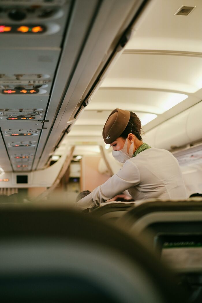 Flight attendant wearing mask performing safety duties inside airplane cabin