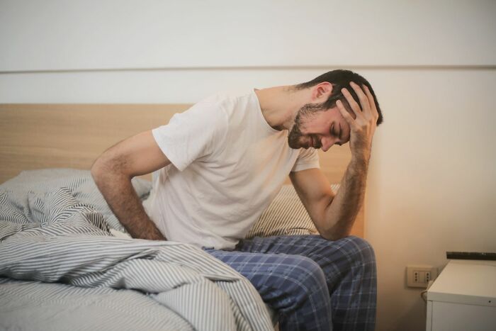 Man sitting on a bed holding his head and back in pain, showing types of pain.
