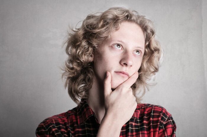 A young man with curly hair looks up thoughtfully, pondering the complexities of growing up in polygamous families.