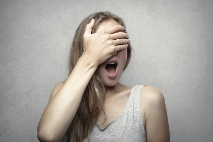 A woman covering her eyes and gasping, reacting to a wild courtroom story.