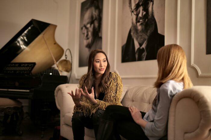 Two women having a serious conversation in a room with portraits
