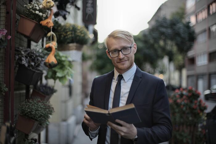 A man in glasses holds an open book, smiling. He wears a suit and tie, embodying advanced English words for smart speakers. A man in glasses holds an open book, smiling. He wears a suit and tie, embodying advanced English words for smart speakers.