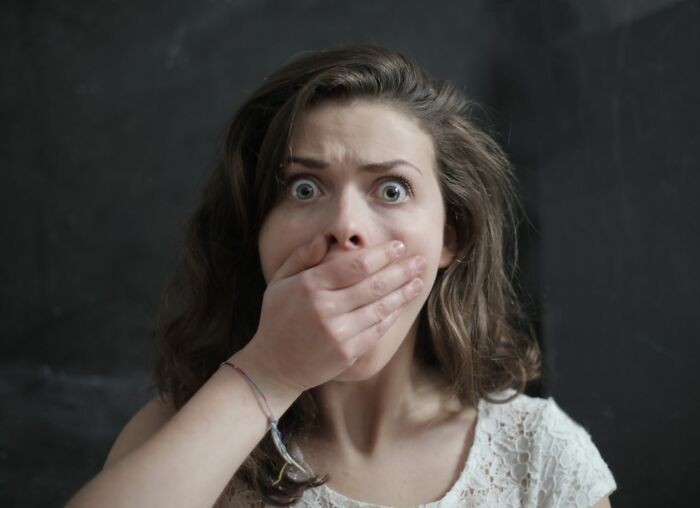 A woman with wide eyes covers her mouth in shock, representing finding worst things on partners phone.