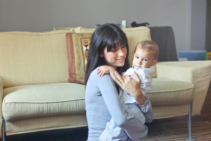 Mother holding smiling baby in living room near beige couch