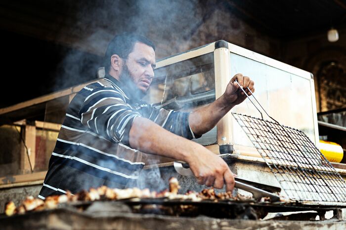 Man cooking barbecue grilling meat surrounded by smoke