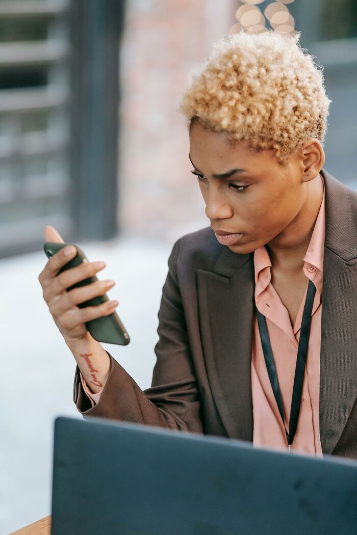 Woman looking suspiciously at phone while working on laptop
