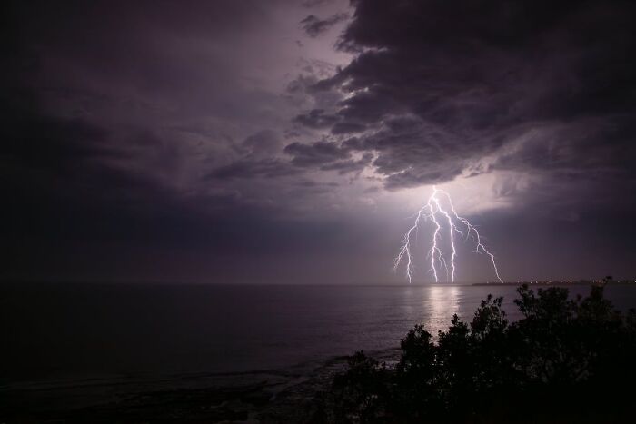 Lightning storm over ocean at night with dark clouds diving story