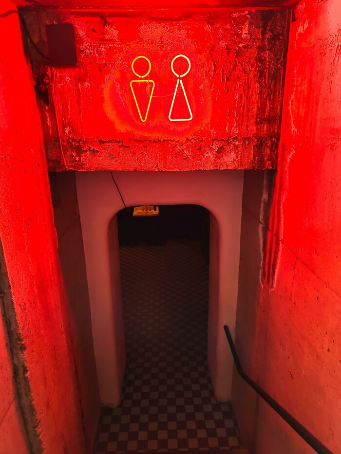 Dimly lit hallway with neon restroom signs in cheating and complete idiots story