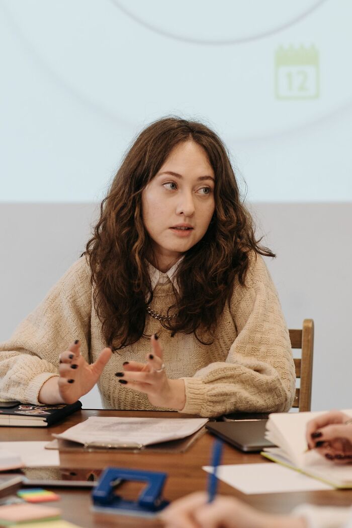 A woman with curly hair, showing hints of being very smart, gestures while talking at a table.