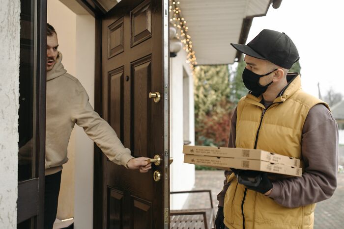 A delivery person in a mask hands pizza boxes to a customer at their doorstep, representing people who hid their true selves.
