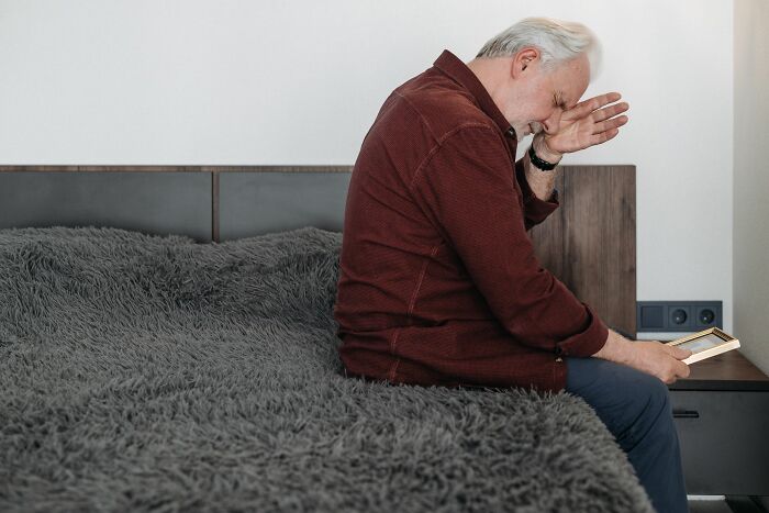 Older man sitting on bed emotional looking at phone