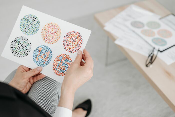 A person holds a color blindness test with Ishihara plates, revealing numbers within colorful dotted circles for a visual challenge.