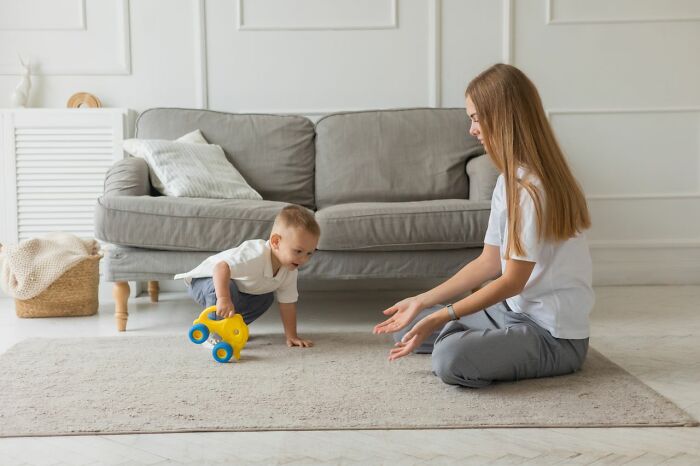 Mother playing on carpet with toddler and toy car at home
