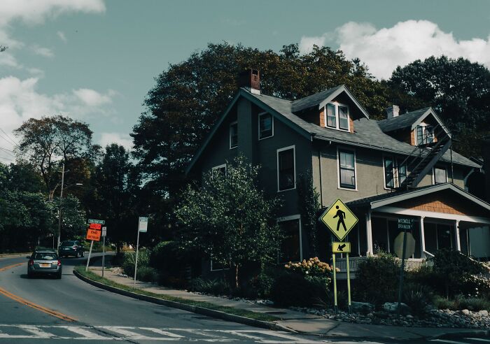 A quaint house on a street corner, with pedestrian signs, suggesting stories about people who hid their true selves.