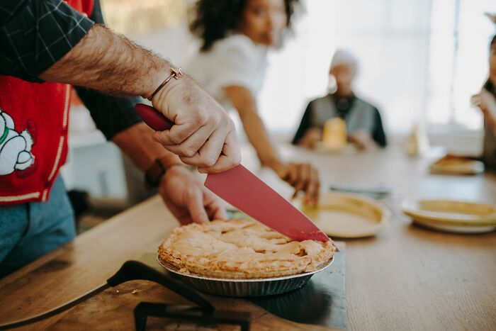 A person with a red sweater using a pink knife to cut a pie, feeling rage mode after not taking it anymore.