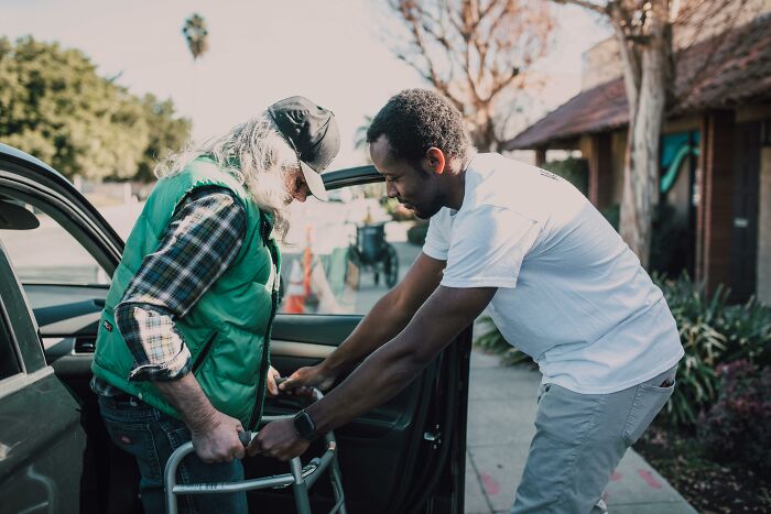 Man helping elderly person with walker into car
