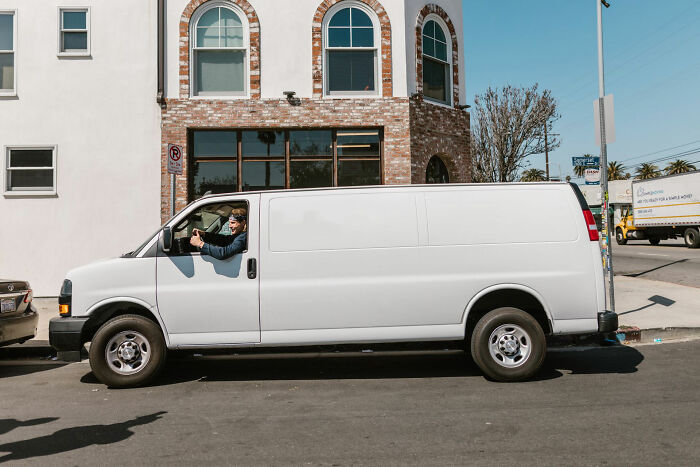 Man driving white van parked on city street in front of brick building