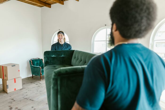 Two men moving a green sofa in a bright room with wooden ceiling