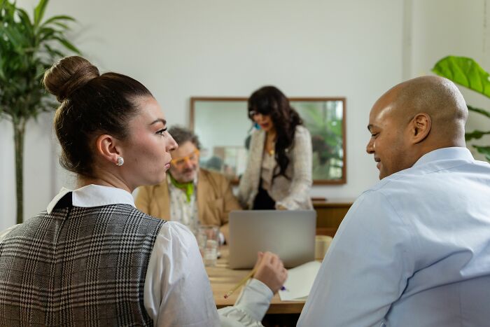 A woman listens intently at a table, a scene that could involve hilariously misread social cues and awkwardness.